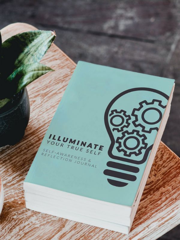 Three copies of the “Illuminate Your True Self” journal are displayed on a table.